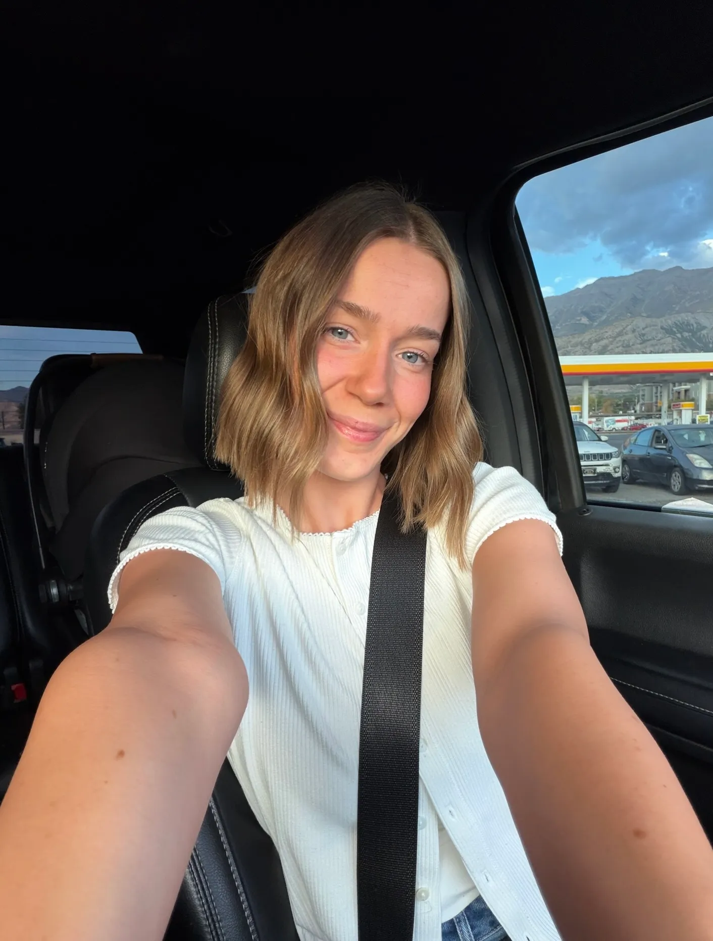 Client smiling in a car selfie in natural light with a soft, golden spray tan